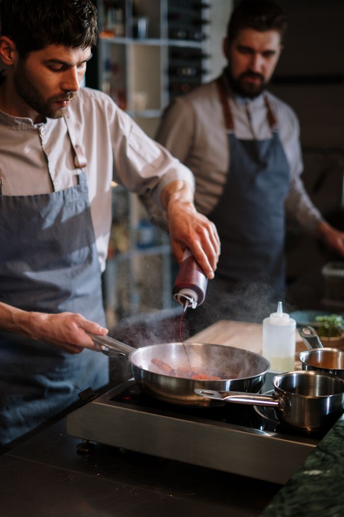 Two chefs in aprons work together in a modern kitchen, preparing food with focus and skill.